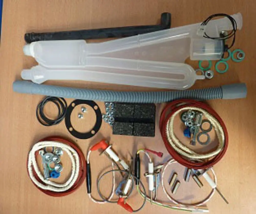 Wartungssatz mit verschiedenen Komponenten, darunter Rohre, Dichtungen und Kabel, übersichtlich auf einem Tisch angeordnet, zur Verwendung in Remeha Heizsystemen.